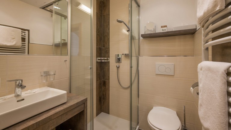 Badkamer met toilet, radiator, wasbak met spiegel en douchecabine.