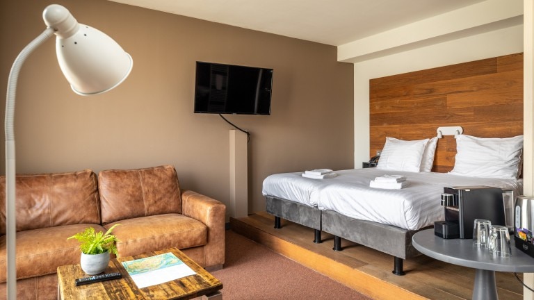 Hotelzimmer mit getrennten Betten, einer Bank, einem Tisch, einem Fernseher und einer Lampe.