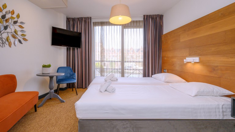 Hotelzimmer mit getrennten Betten, einer Bank, einem Stuhl und Fernseher.