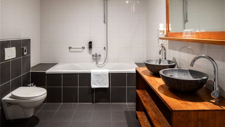 Badkamer met bad, toilet en dubbele wastafel.