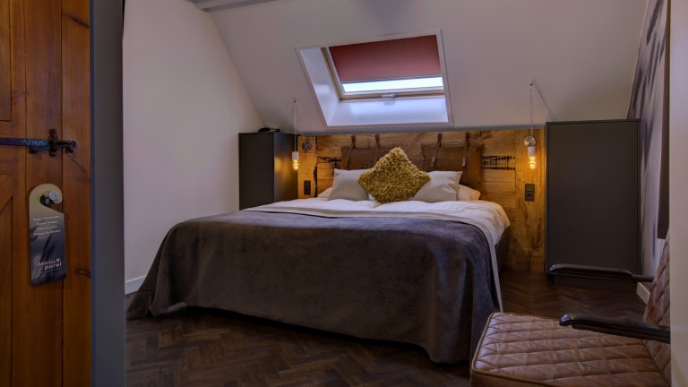 Hotelzimmer mit zwei Betten, einem schrägen Dach, einem Fenster und einem Stuhl.