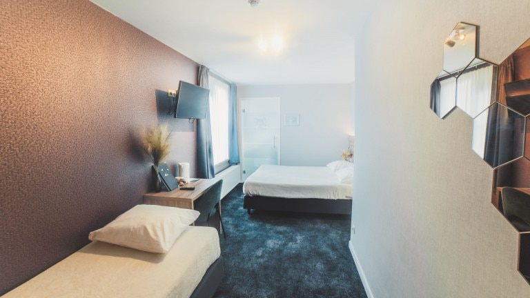 Hotelkamer met drie gescheiden bedden, een televisie en hexagon spiegels.